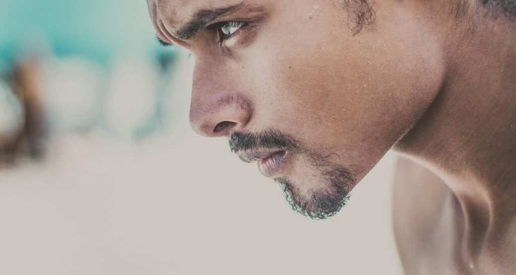 The image shows a young man with a goatee staring off camera with determination. The background is completely blurred out indicating a state of focus.