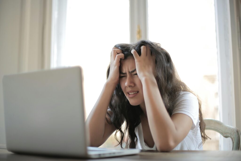 The image shows a woman, hands in her hair, staring at a laptop in frustration. The implication is Social Media is making her stressed.