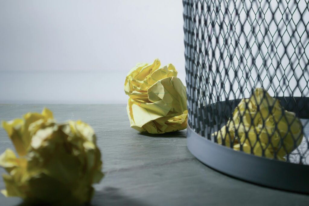 The image shows three yellow, crumpled pieces of paper, two outside of a grid bin, one inside the bin.